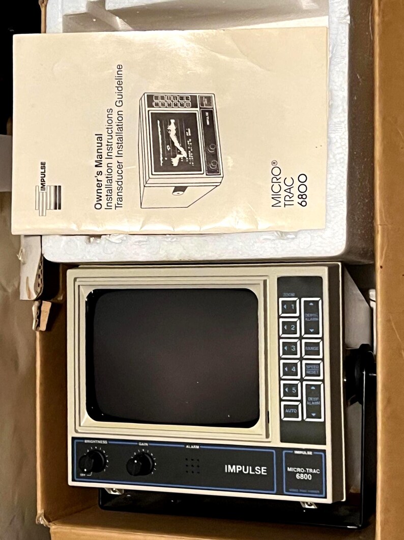 May include: An Impulse Micro-Trac 6800 marine fish finder unit with a beige casing, a black screen, and a control panel featuring buttons and knobs. Included is an owner's manual titled Owner's Manual Installation Instructions Transducer Installation Guideline.