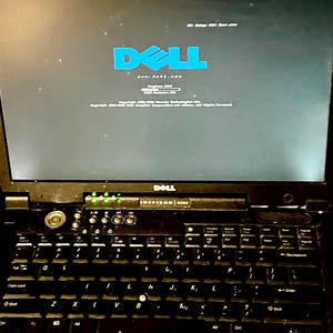 Könnte beinhalten: Ein schwarzer Dell Inspiron 4300 Laptop, der ein blaues Dell-Logo und Boot-Text auf dem Bildschirm anzeigt. Die Tastatur verfügt über schwarze Tasten mit weißer Beschriftung, einen runden Einschaltknopf und grüne Statusanzeigen.