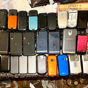 May include: A collection of various used cell phones, including models from LG, Motorola, and Samsung. The phones are in different colors, including black, orange, blue, and silver. Some phones have visible wear and tear.