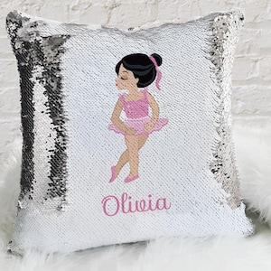 May include: A white and silver sequin pillow with a pink ballerina illustration and the name "Olivia" printed in pink.