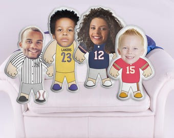 May include: Four custom-made pillows with faces printed on them. Each pillow is dressed in a different sports uniform. The pillows are sitting on a white couch.