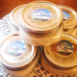 May include: Several glass jars with silver lids are stacked on a floral patterned surface. Each jar has a label with the words "Graceful Nature" and a scent name: Lavender, Sandalwood Rose, or Rosemary Sage. The jars are filled with a creamy substance.
