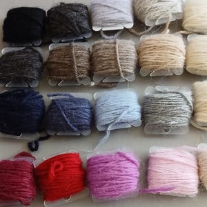 Puede incluir: Una colección de carretes de hilo en varios colores, incluyendo negro, gris, marrón, azul, rojo y rosa. El hilo está enrollado en pequeños carretes de plástico, mostrando una gama de texturas y tonos adecuados para proyectos de manualidades.