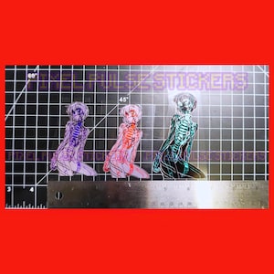 Könnte beinhalten: Drei Aufkleber mit einer knienden Anime-Figur mit sichtbaren Skelettstrukturen. Die Aufkleber sind in Lila, Rot und Türkis gehalten, mit dem Text "PIXEL PULSE STICKERS" im Hintergrund. Unter den Aufklebern befindet sich ein Lineal.