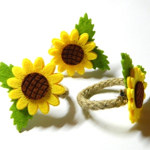 May include: Three felt sunflower napkin rings with brown centers and green leaves. The rings are made of natural twine.