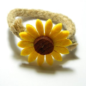 May include: A yellow felt sunflower with a brown center is attached to a brown jute rope ring.