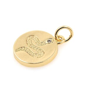 May include: Gold-toned pendant charm featuring a snake design with a small clear stone for an eye. The charm is round and has a loop for attaching to a necklace or bracelet.