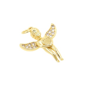 May include: Gold-tone charm featuring a winged cherub holding a heart, adorned with clear sparkling stones.