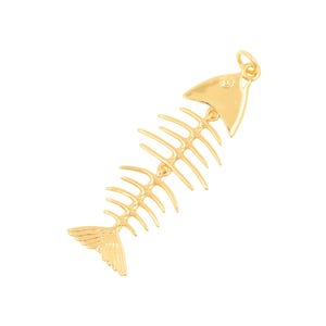 以下が含まれることがあります： 魚の骨の形をしたゴールドトーンの金属製ペンダント。三角形の頭部、中央の背骨、外側に伸びる複数の肋骨のような突起が特徴で、扇形の尾で終わっています。上部には小さな丸いループが付いています。