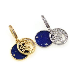 May include: Two pairs of earrings. One pair is gold-toned, the other is silver-toned. Each earring features a small, dark blue disc with white stars, paired with a circular charm. The gold charm has a tree design, while the silver charm has a tree design with clear stones.