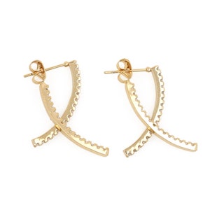 以下が含まれることがあります： クロスデザインのゴールドフープイヤリングのペア。イヤリングは小さなクリアストーンで飾られています。