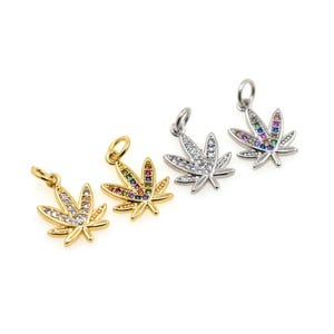 May include: Four leaf-shaped pendants. Two are gold-coloured, one with clear and rainbow-coloured stones. The other two are silver-coloured, one with clear stones and the other with rainbow-coloured stones. Each pendant has a small loop at the top for attaching.