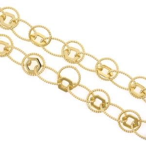 May include: Close-up of two gold-coloured chain necklaces. The chains feature a repeating pattern of hexagonal and circular links. The links are connected by smaller, twisted rope-like chain segments. The jewellery is set against a white background.