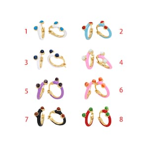 Puede incluir: Ocho pares de pendientes de aro con diferentes colores de esmalte y detalles de piedras preciosas. Los pendientes están numerados del 1 al 8.