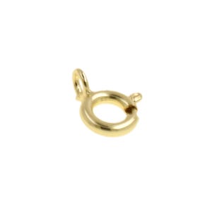 May include: A close-up of a small, gold-colored spring ring clasp. The clasp is circular with a small loop on one side and a lever on the other for opening and closing. The metal has a shiny finish.