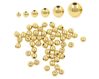 May include: A collection of gold-colored metal beads in various sizes, scattered on a white background. The beads range from small to large, with a polished, reflective surface. These beads are ideal for jewelry making and crafting.