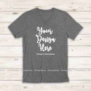 May include: A heather gray V-neck t-shirt mockup with the text "Your Design Here" and "Mockup by MockupStation" printed on the front.