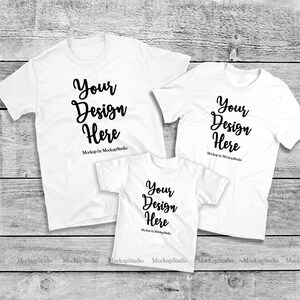 Peut inclure: Trois t-shirts blancs avec le texte "Your Design Here" en noir sur chaque t-shirt. Les t-shirts sont disposés sur une surface en bois.