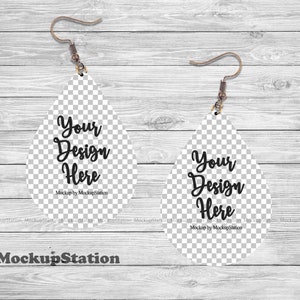 K&ouml;nnte beinhalten: Ein Mockup eines Paares tropfenf&ouml;rmiger Ohrringe mit transparentem Hintergrund. Die Ohrringe sind wei&szlig; und haben einen silbernen Haken. Der Text "Your Design Here" ist auf jedem Ohrring geschrieben. Der Text "Mockup by MockupStation" ist unter dem Text auf jedem Ohrring geschrieben.