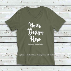 May include: A plain olive green v-neck t-shirt with short sleeves. The shirt has the text "Your Design Here" in white on the front. Mockup by MockupStation.