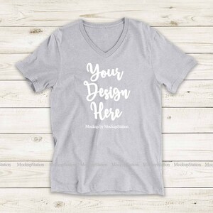 May include: A gray V-neck t-shirt with the text "Your Design Here" and "Mockup by MockupStation" printed on the front.