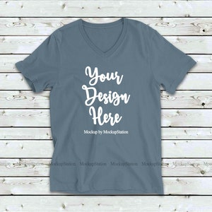 May include: A plain, light blue v-neck t-shirt mockup on a wood background. The text "Your Design Here" is printed on the shirt. "Mockup by MockupStation" is printed below the text.