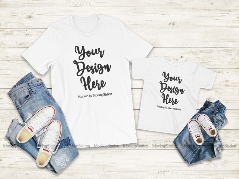 K&ouml;nnte beinhalten: Zwei wei&szlig;e T-Shirts mit dem Text "Your Design Here" auf einem wei&szlig;en Holzgrund. Die T-Shirts liegen auf einer blauen Jeans und wei&szlig;en Turnschuhen.