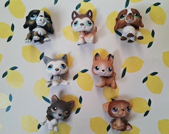 Puede incluir: Colección de siete pequeñas figuras de perros coloridos. Los perros tienen varios colores de pelaje, incluyendo marrón, blanco, gris y negro. Tienen ojos grandes y expresivos y están en diferentes poses. El fondo es un patrón amarillo claro con ilustraciones de limones.