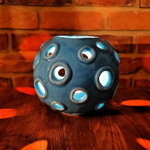 May include: A blue ceramic candle holder with a spherical shape and multiple circular cutouts. The candle holder is sitting on a wooden surface.