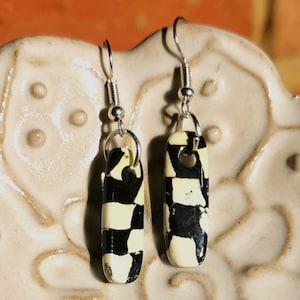 Puede incluir: Un par de pendientes colgantes con patrones geométricos en blanco y negro en el colgante. Los pendientes están hechos de metal y tienen un acabado plateado.