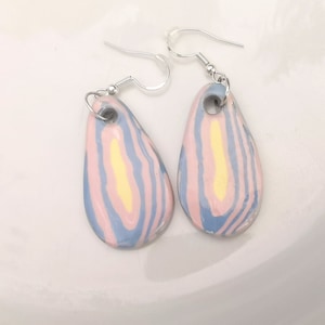 Peut inclure: Une paire de boucles d'oreilles en forme de goutte d'eau avec un motif marbré rose, jaune et bleu. Les boucles d'oreilles ont des crochets argentés.