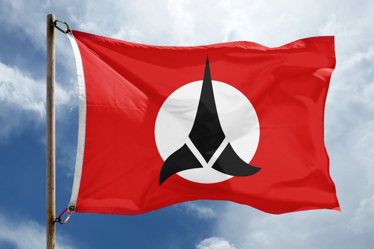 Flag of the Klingon Empire waving on a flag pole on a partly-cloudy day.