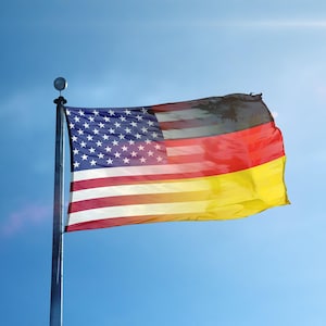 Könnte beinhalten: Eine Flagge, die das Design der amerikanischen und deutschen Flaggen kombiniert und vor einem klaren blauen Himmel weht. Die amerikanische Seite zeigt Sterne und Streifen, während die deutsche Seite schwarze, rote und gelbe Streifen zeigt.