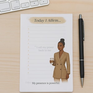 May include: A notepad with the text "Today I Affirm..." and a line for affirmations. An illustration of a person in a tan blazer holding a coffee cup is on the notepad. A black pen and a white keyboard are also in the image.