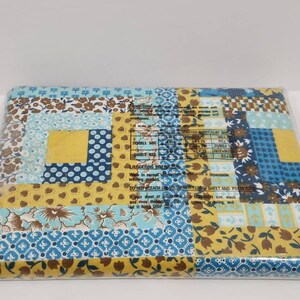 May include: A packaged blue and yellow patchwork quilt fabric with a floral pattern. The fabric is packaged in a clear plastic bag. The package includes a label with the text "DOUBLE BED", "FLAT SHEET", "LAUNCERING INSTRUCTIONS", "DO NOT BLEACH UNICOBAR FLORAL SHEET AND PADNICASE", "If your sheet or pad is a fitted one, wash and rinse it before placing it in the dryer, and let it hang to dry."