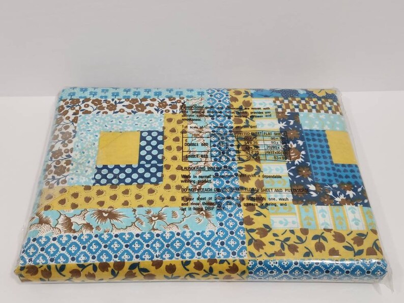 May include: A packaged blue and yellow patchwork quilt fabric with a floral pattern. The fabric is packaged in a clear plastic bag. The package includes a label with the text "DOUBLE BED", "FLAT SHEET", "LAUNCERING INSTRUCTIONS", "DO NOT BLEACH UNICOBAR FLORAL SHEET AND PADNICASE", "If your sheet or pad is a fitted one, wash and rinse it before placing it in the dryer, and let it hang to dry."