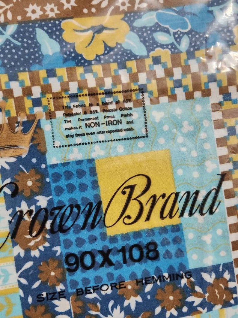 May include: A blue and brown fabric with a floral pattern. The fabric is labeled "Crown Brand" and has a size of 90x108 inches. The label also states that the fabric is a blend of 66% polyester and 35% percale cotton and is non-iron.