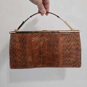 Cartera de mano retráctil con asa rígida y parte superior en color marrón coñac y diseño de piel de serpiente con cierre a presión