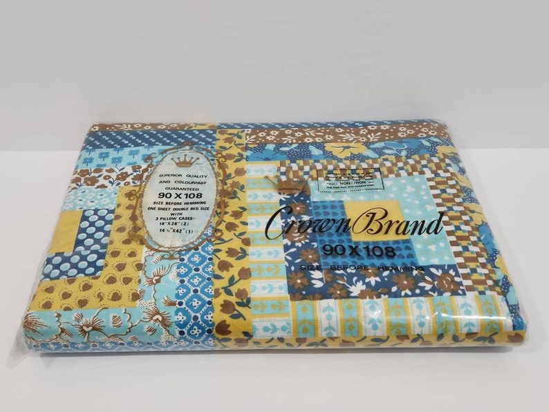 May include: A package containing a blue and yellow patchwork patterned bed sheet set. The package label reads "Crown Brand 90 x 108" and "Superior Quality Any Colourfast Guaranteed".