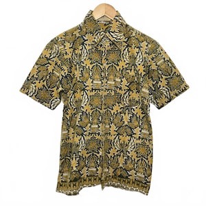 May include: Short-sleeved shirt with a striking floral design in gold, black, and white. The shirt is displayed on a wooden hanger, highlighting its detailed pattern and cut. The fabric of the shirt looks lightweight and suitable for warmer weather.