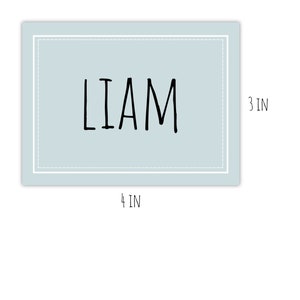Op de afbeelding: Een lichtblauw gepersonaliseerd naamschild met een witte rand en de naam "LIAM" in zwarte schrift. Het schild is 10,16 cm breed en 7,62 cm hoog.