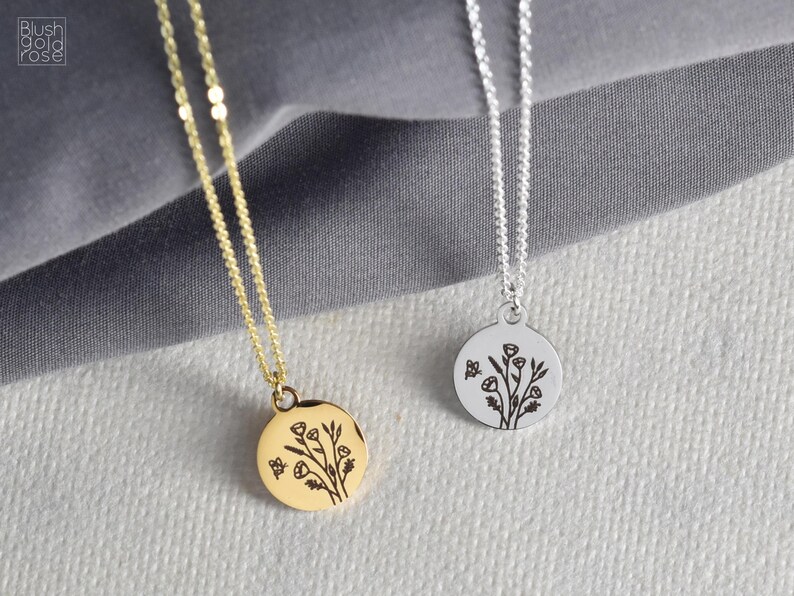 May include: Two delicate necklaces with round pendants. One is gold-toned, the other silver-toned. Each pendant features a floral design with a small butterfly. The necklaces are displayed on a textured, light gray surface.