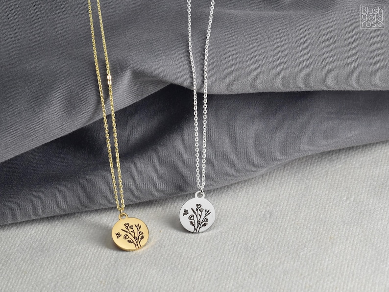 May include: Two delicate necklaces with round pendants. One is gold-toned, the other silver-toned. Each pendant features a floral design. The necklaces hang against a gray fabric background, showcasing the jewelry's details and design.
