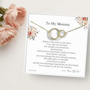 May include: A gold-toned necklace featuring two interlocking circular pendants on a display card. The card includes the text To My Mommy and a poem about the bond between parent and child, decorated with floral illustrations in shades of pink and green.