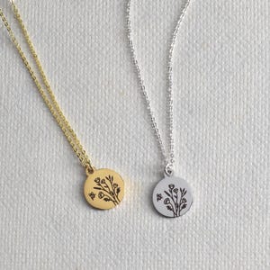 May include: Two delicate necklaces with floral pendant designs. One necklace is gold-toned, the other is silver-toned. Each pendant features a detailed botanical illustration. The chains are fine and elegant, suitable for everyday wear.