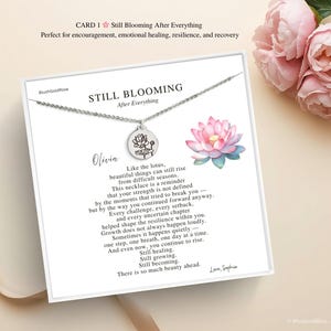 May include: A silver necklace with a round pendant featuring a lotus flower design, displayed on a white card with text. The card reads "Still Blooming After Everything" and includes a watercolor lotus flower illustration. Pink roses are in the background.
