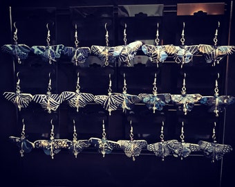 May include: A display of butterfly-shaped earrings with black and white patterns and blue accents. The earrings are hanging from a silver wire.