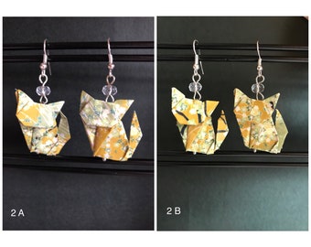 May include: Two pairs of origami cat earrings. The cats are made of yellow and green patterned paper. The earrings are hanging from silver hooks.