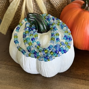 May include: A stack of colorful beaded bracelets in shades of blue, green, and white. The bracelets are made of small, round beads and are arranged in a circular pattern.
