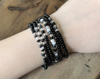 May include: A set of six black and white beaded bracelets. The bracelets are made with small, round beads and are stacked on a person's wrist.